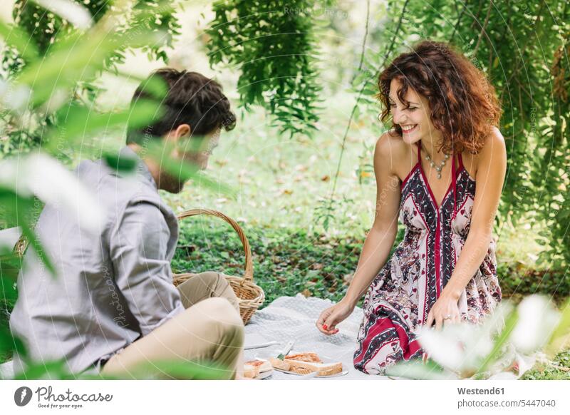 Happy couple having a picnic in a park smiling smile twosomes partnership couples Picnic picnicking parks people persons human being humans human beings Meals