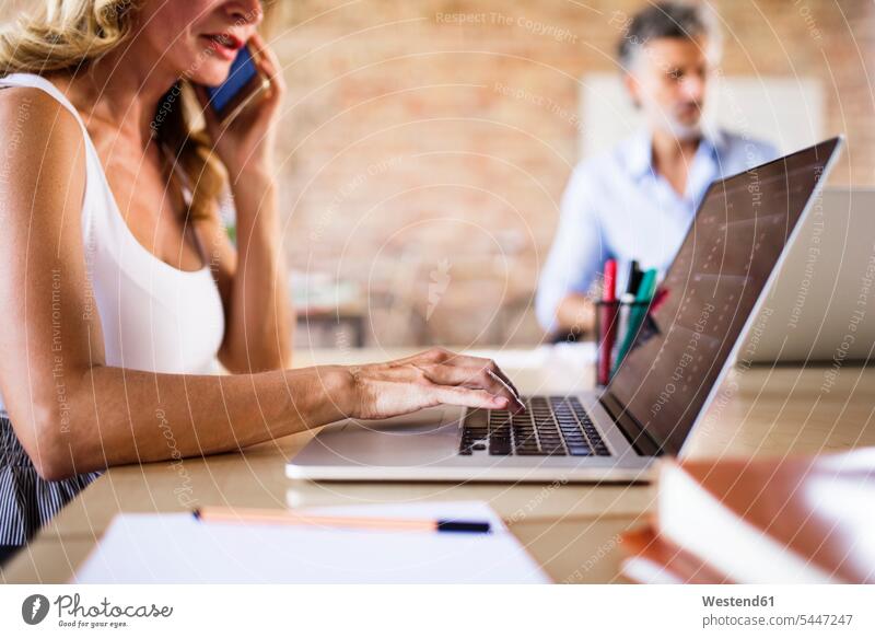 Businesswoman using cell phone and laptop at desk in office working At Work offices office room office rooms Laptop Computers laptops notebook desks Businessman