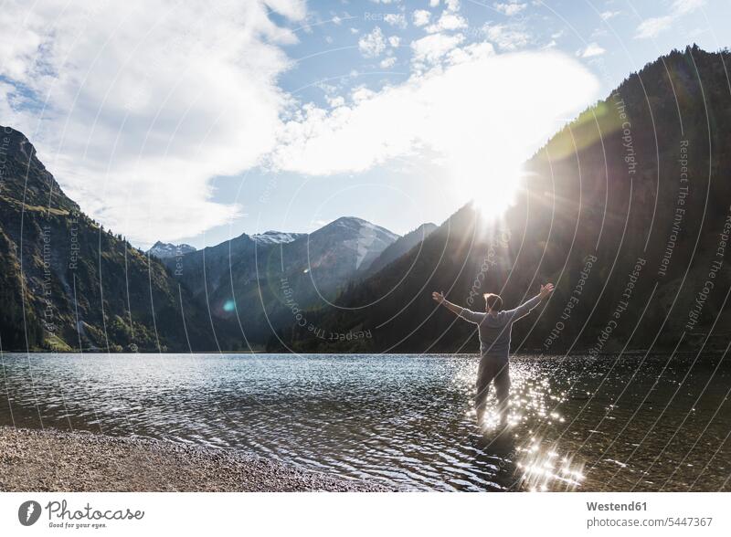 Austria, Tyrol, hiker standing with outstretched arms in mountain lake wanderers hikers mountain lakes man men males hiking mountains water waters body of water