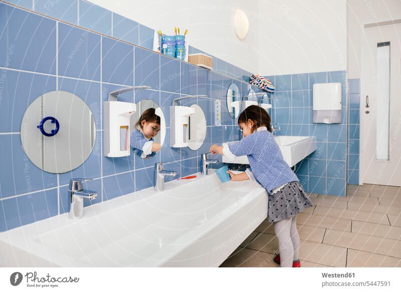 Little girl using water for brushing her teeth in bathroom of a kindergarten females girls nursery school child children kid kids people persons human being