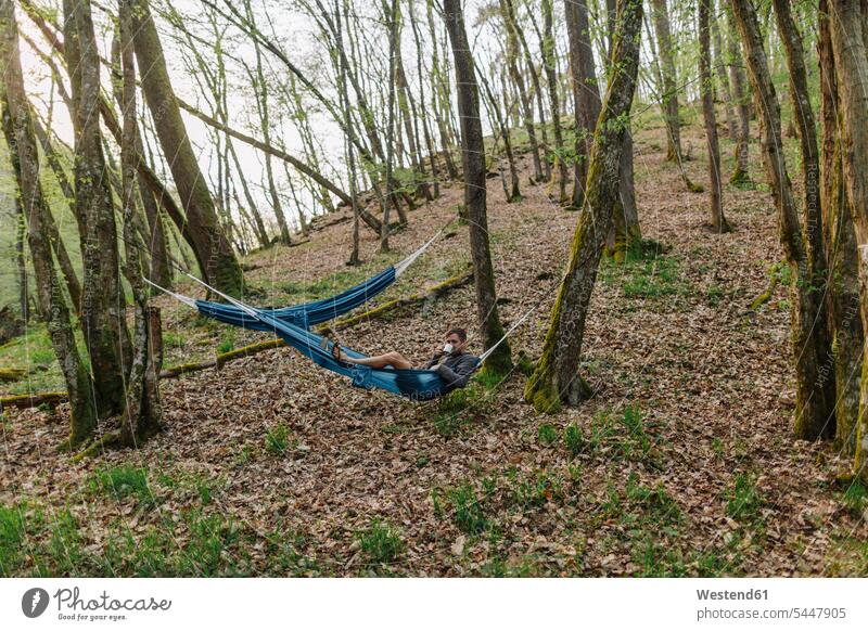 Germany, Rhineland-Palatinate, Vulkan Eifel, young man lying in hammock in forest men males getting away from it all Getting Away From All unwinding relaxing