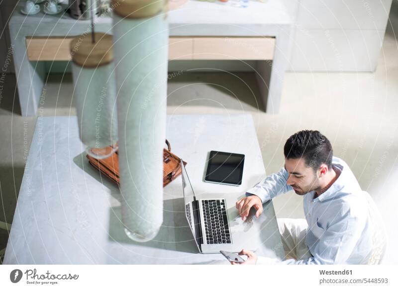 Young businessman working in office, using mobile devices sitting Seated text messaging SMS Text Message At Work desk desks laptop Laptop Computers laptops