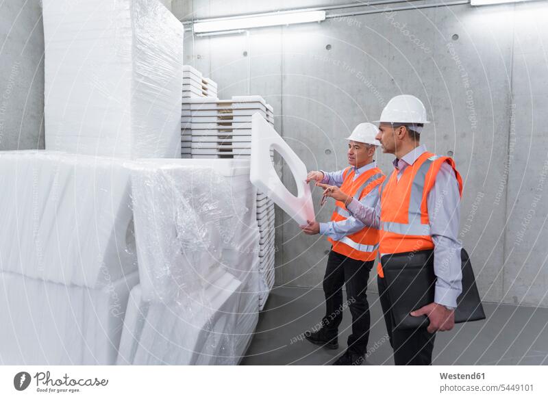 Two colleagues wearing safety vests and hard hats examining polystyrene - a  Royalty Free Stock Photo from Photocase