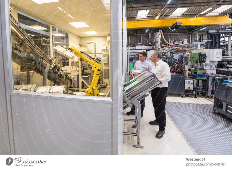 Two men talking in factory shop floor looking at industrial robot speaking colleagues factories man males Adults grown-ups grownups adult people persons