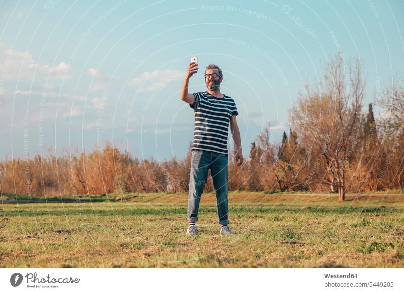 Man standing on a meadow taking photo with smartphone Selfie Selfies man men males Adults grown-ups grownups adult people persons human being humans