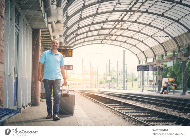 Smiling man with luggage on platform train station men males Adults grown-ups grownups adult people persons human being humans human beings walking going