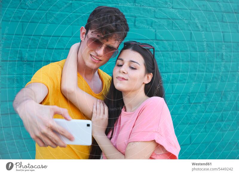 Young couple taking selfie with smartphone in front of blue brick wall twosomes partnership couples Selfie Selfies Smartphone iPhone Smartphones people persons