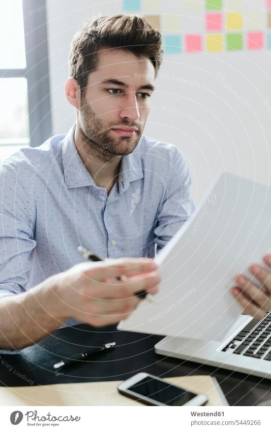 Young businessman working in office, reading documents At Work offices office room office rooms Smartphone iPhone Smartphones Businessman Business man