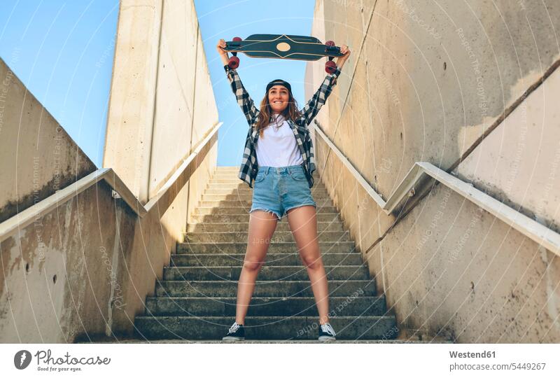 Portrait of happy young woman standing on staircase holding up her longboard female skateboarder female skater female skateboarders females women skaters people