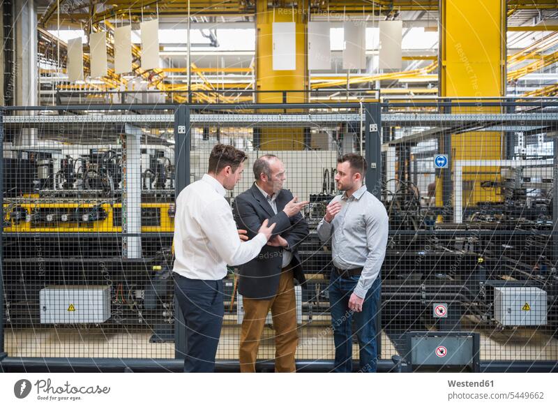 Three men talking in factory shop floor factories man males speaking colleagues working At Work Adults grown-ups grownups adult people persons human being