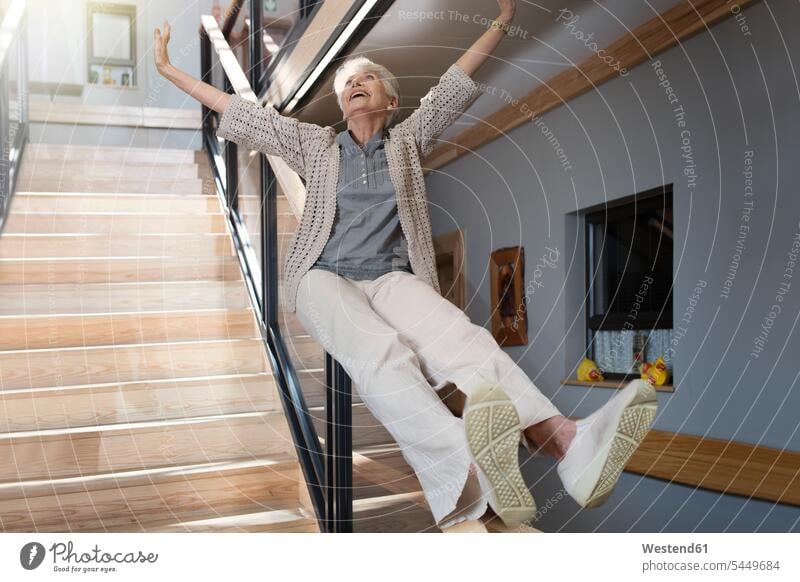 Happy senior woman sliding down a staircase senior women elder women elder woman old Railing Railings slide retirement home nursing home stairs stairway