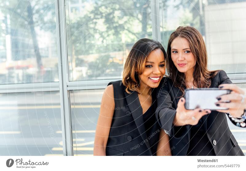 Two women taking a selfie in the city Selfie Selfies mobile phone mobiles mobile phones Cellphone cell phone cell phones woman females female friends telephones