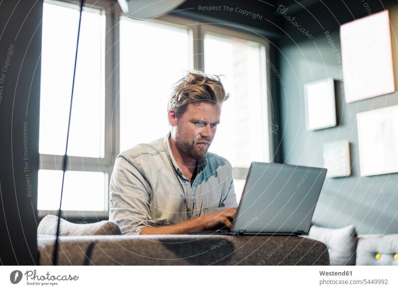 Businessman in lounge area of an office using laptop Business man Businessmen Business men Laptop Computers laptops notebook lounges Lounge Room offices