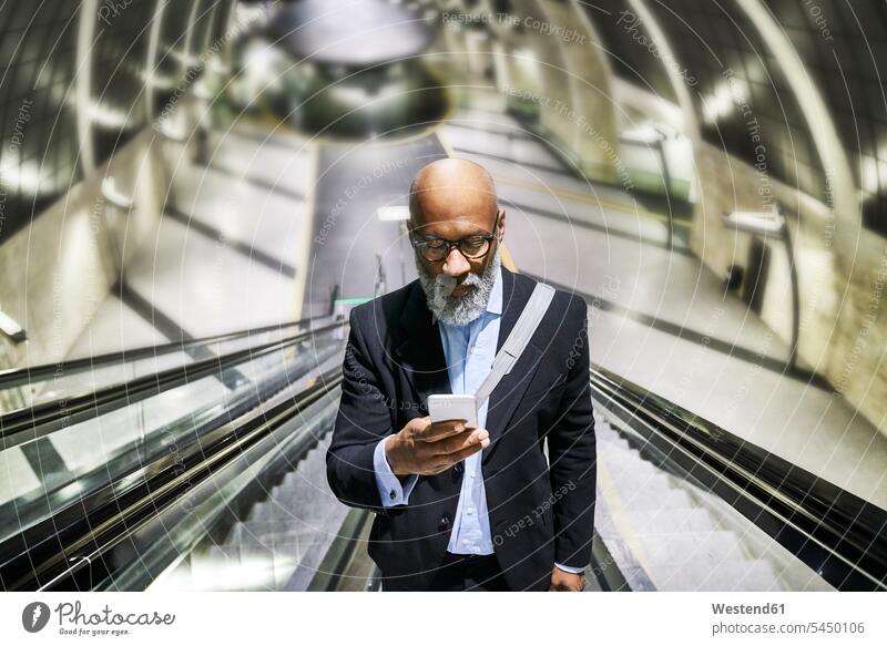 Businessman with smartphone reading messages on escalator on the move on the way on the go on the road text messaging SMS Text Message Smartphone iPhone