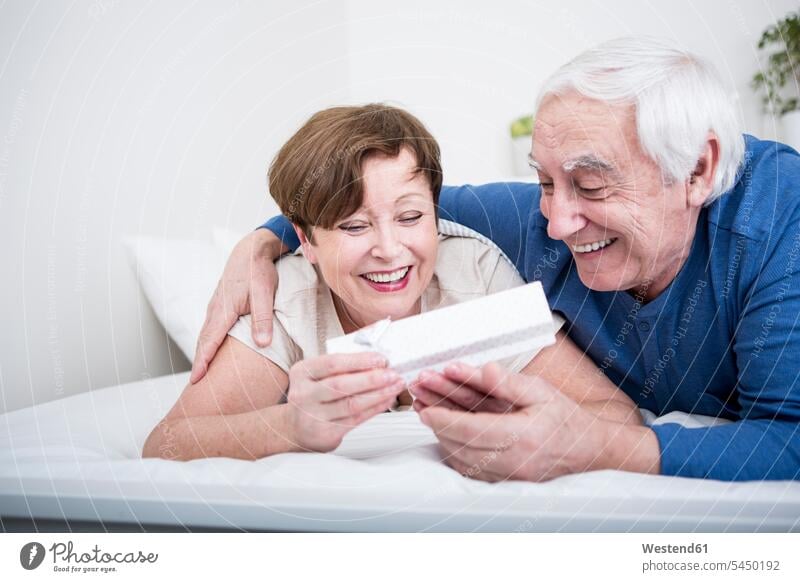 Senior couple lying in bed, man giving present to woman caucasian caucasian ethnicity caucasian appearance european bonding carefree beds relationship