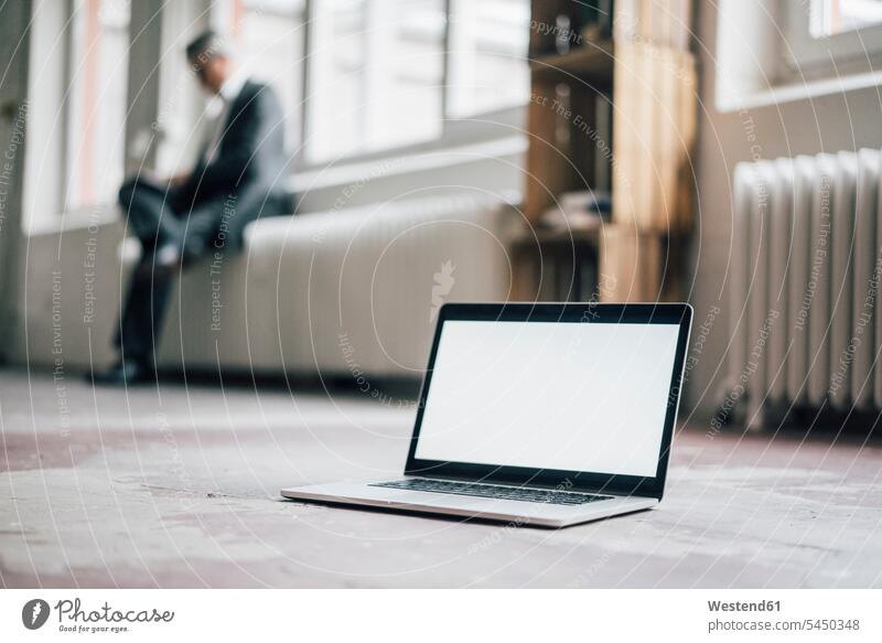 Laptop on floor with businessman in background laptop Laptop Computers laptops notebook sitting Seated floors Businessman Business man Businessmen Business men