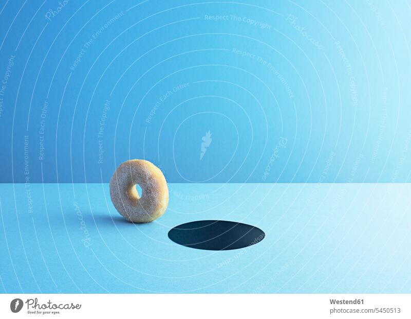 Doughnut and hole on light blue ground single object 1 one baked goods pastries rolling blue background blue backgrounds icing sugar powdered sugar doughnut