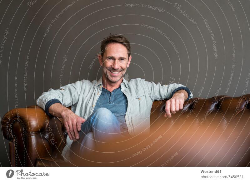 Portrait of smiling mature man sitting on leather couch portrait portraits men males Adults grown-ups grownups adult people persons human being humans