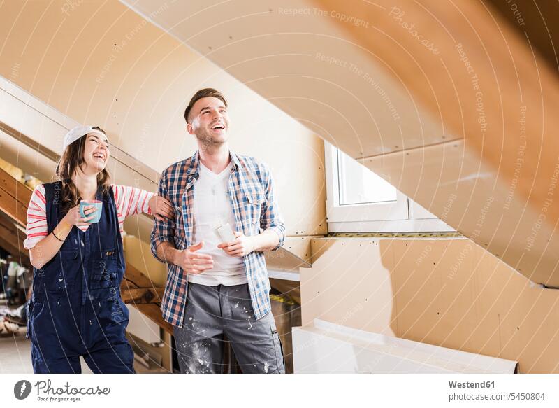 Young couple on construction site of their new home, looking at construction plan renovation renovate refurbish refurbishing Renovations redecorating renovating