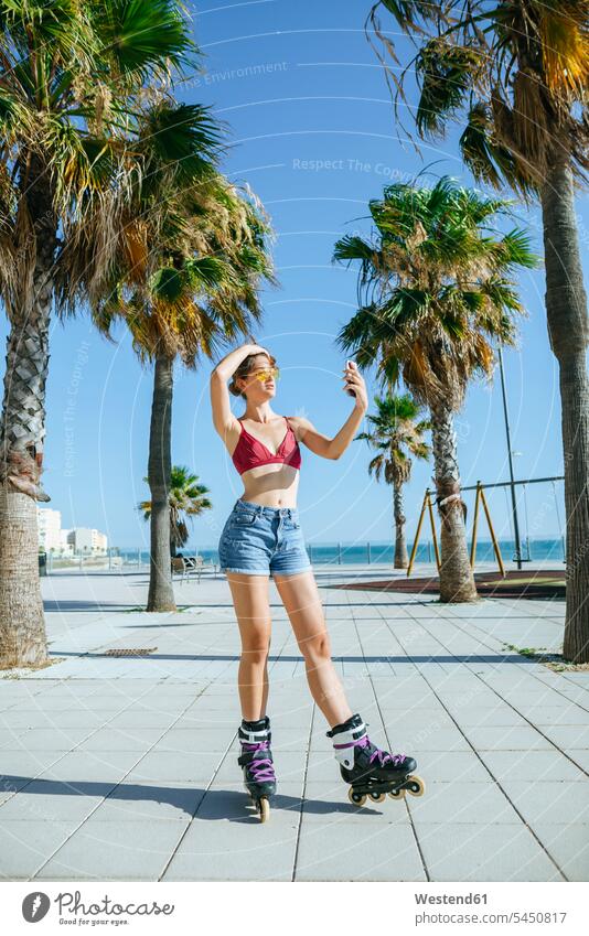 Young woman on inline skates taking a selfie on boardwalk inliners mobile phone mobiles mobile phones Cellphone cell phone cell phones Palm Palm Trees Palms