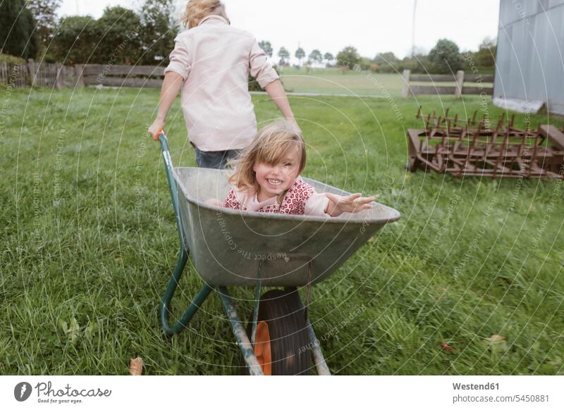 Boy pulling wheelbarrow with his little sister through the garden girl females girls hand barrow pushcart wheelbarrows hand barrows wheel barrow child children