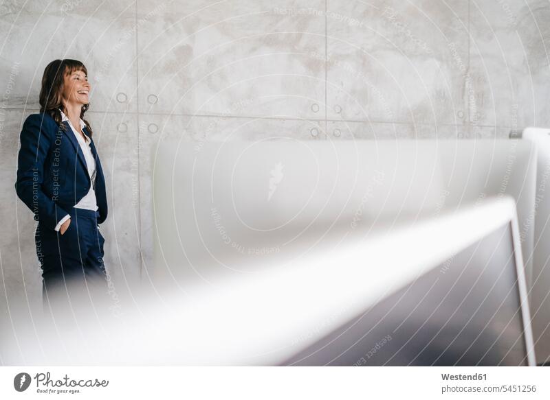 Businesswoman leaning against office wall with hands in pockets females women standing confidence confident technology technologies Technological computer