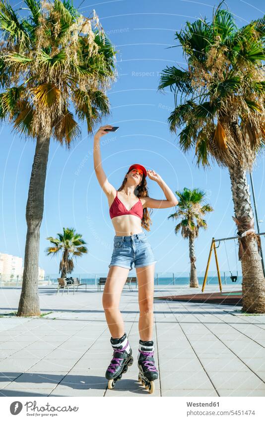 Young woman on inline skates taking a selfie on boardwalk Selfie Selfies mobile phone mobiles mobile phones Cellphone cell phone cell phones Palm Palm Trees