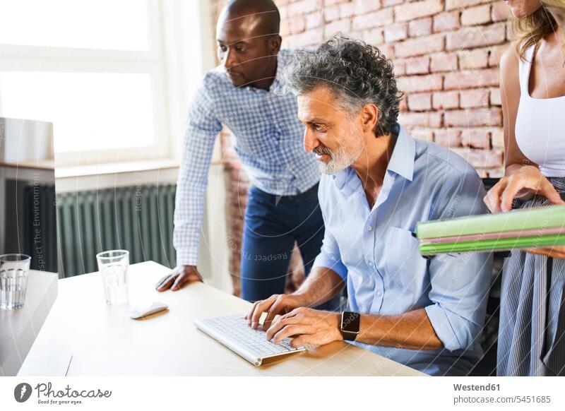 Smiling colleagues working together at desk in office offices office room office rooms At Work desks workplace work place place of work Table Tables workspace