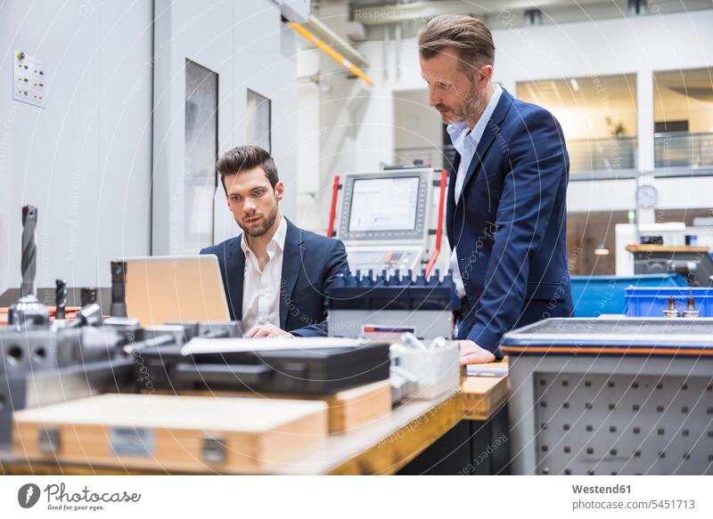 Two men at table in factory using laptop colleagues factories Laptop Computers laptops notebook Businessman Business man Businessmen Business men computer