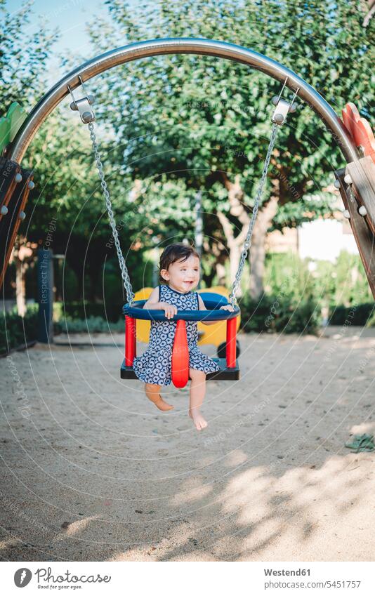 Happy baby girl sitting in swing on playground swing set swingset infants nurselings babies baby girls female people persons human being humans human beings