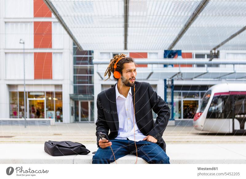 Young businessman with dreadlocks listening music with headphones and cell phone at station Businessman Business man Businessmen Business men headset
