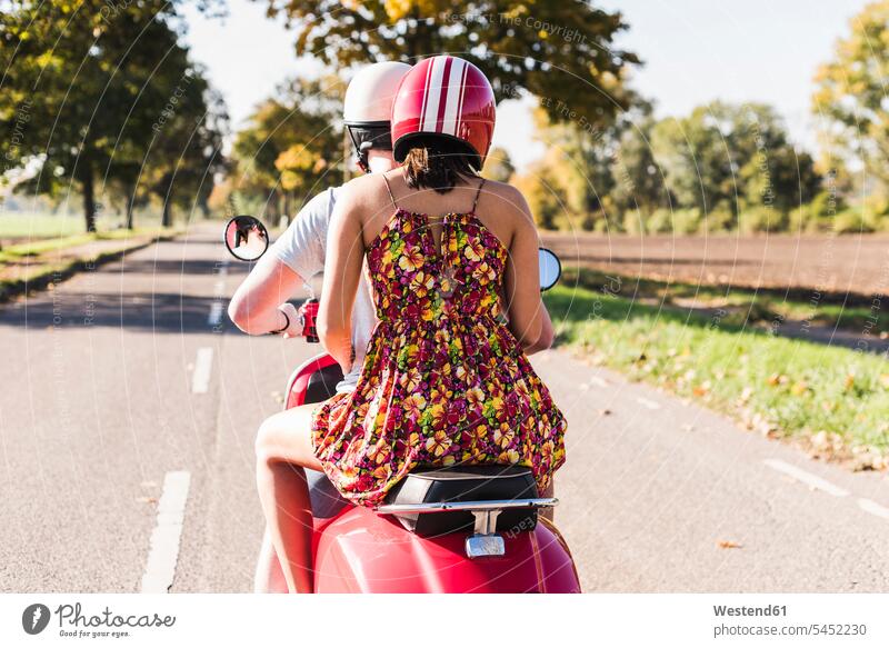 Young couple riding motor scooter on country road rural road rural roads country roads twosomes partnership couples motor-scooter streets transportation people