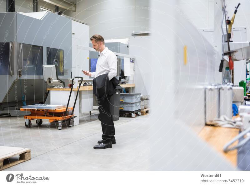 Businessman in factory shop floor looking on the phone factories Business man Businessmen Business men males mobile phone mobiles mobile phones Cellphone