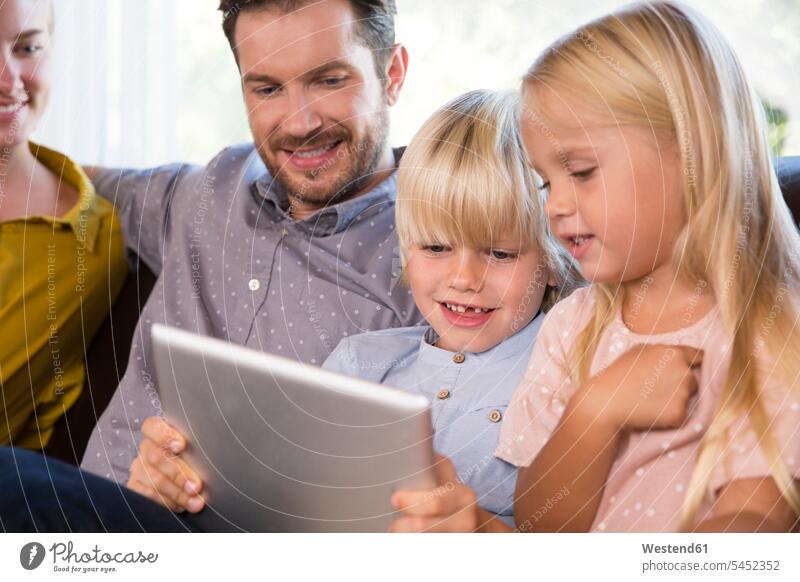 Family sitting on couch at home using tablet settee sofa sofas couches settees digitizer Tablet Computer Tablet PC Tablet Computers iPad Digital Tablet