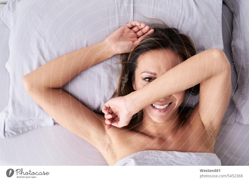 Portrait of smiling woman lying in bed hiding her face laying down lie lying down females women portrait portraits beds hide smile faces Adults grown-ups