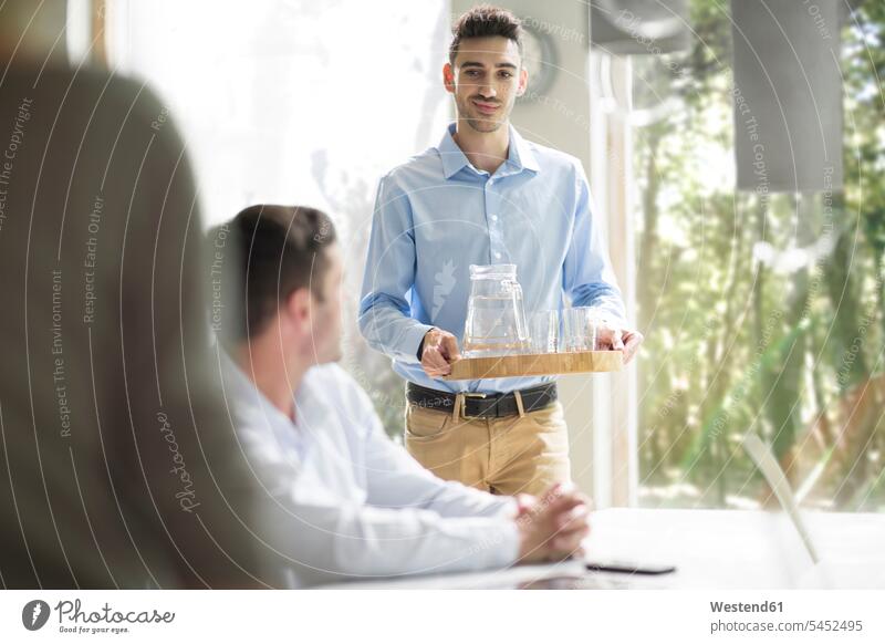 Young man serving water at a business meeting caucasian caucasian ethnicity caucasian appearance european Cooperation working together collaboration Cooperating