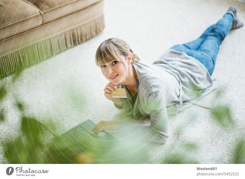 Smiling woman lying on the floor with credit card and laptop debit card laying down lie lying down floors females women smiling smile Laptop Computers laptops