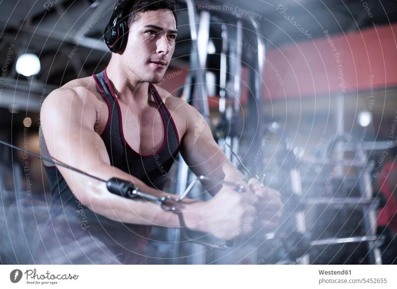 Focused male using cable exercise equipment at gym exercising training practising man males gyms Health Club Adults grown-ups grownups adult people persons