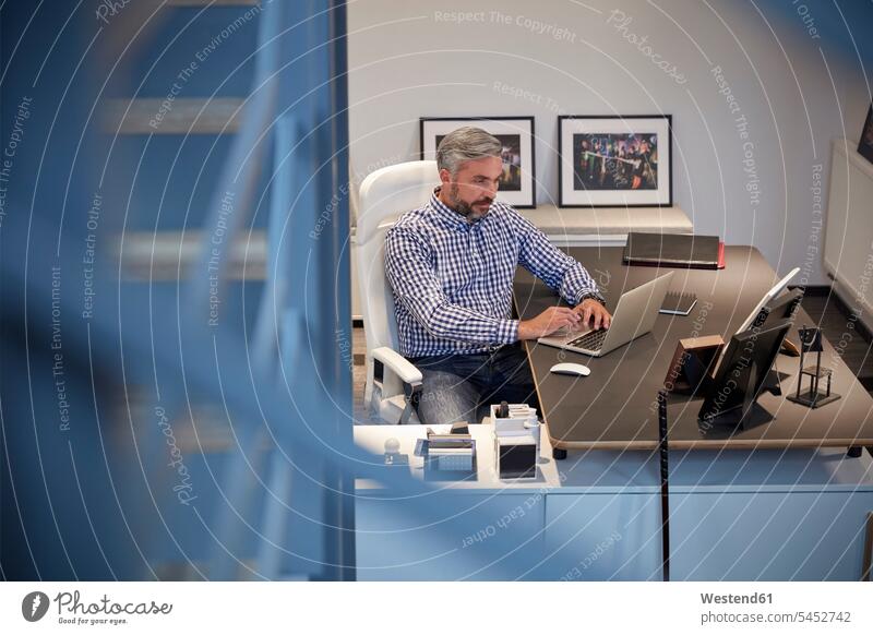 Businessman sitting in office working on laptop Laptop Computers laptops notebook using laptop using a laptop Using Laptops At Work modern contemporary Seated