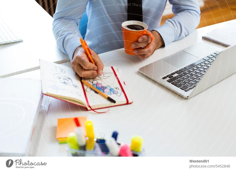 Man drawing into notebook at desk in office sketching desks notebooks offices office room office rooms Table Tables workplace work place place of work business