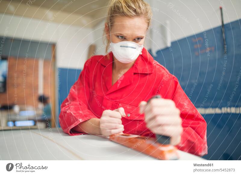 Surfboard shaper workshop, female surfshop employee wearing overalls and mask sanding surfboard surfboards working At Work woman females women grinding abrading