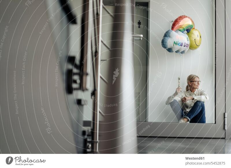 Businesswoman sitting on corridor holding balloon Seated businesswoman businesswomen business woman business women balloons portrait portraits business people