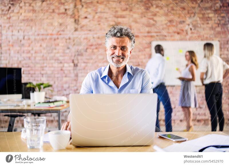 Portrait of smiling businessman in office with colleagues in background offices office room office rooms portrait portraits smile Businessman Business man