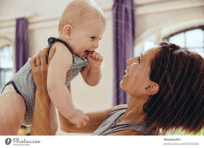 Sporty woman lifting up happy baby in training room exercising exercise practising laughing Laughter infants nurselings babies mother mommy mothers mummy mama