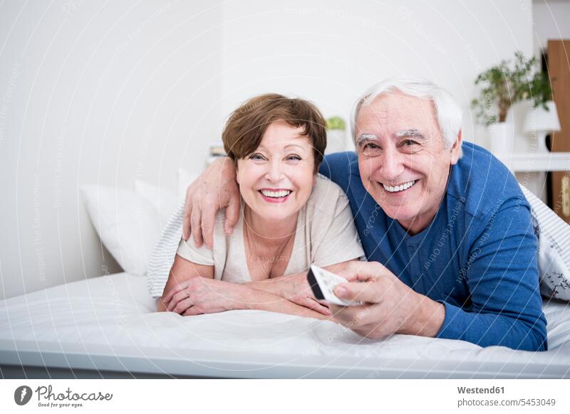 Senior couple lying in bed with remote control caucasian caucasian ethnicity caucasian appearance european carefree beds relationship Human Relationship smiling