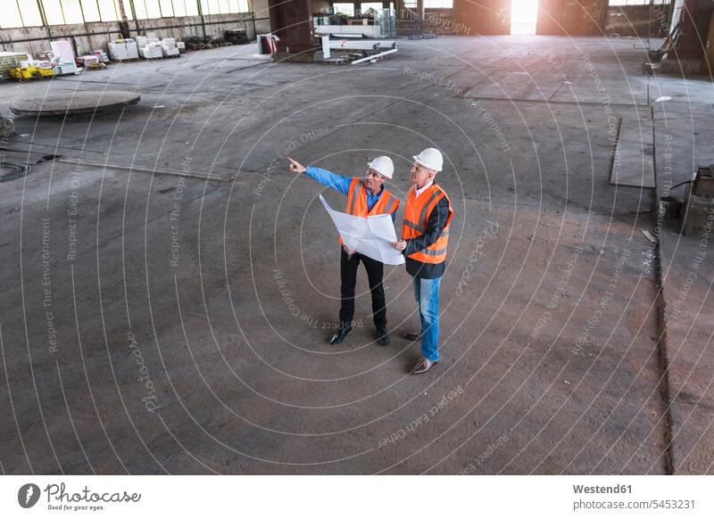 Two colleagues wearing safety vests and hard hats talking in a building - a  Royalty Free Stock Photo from Photocase