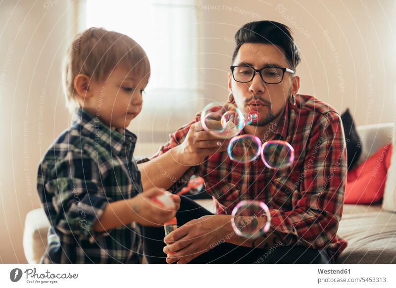 Father and son blowing soap bubbles at home sons manchild manchildren father pa fathers daddy dads papa playing family families people persons human being