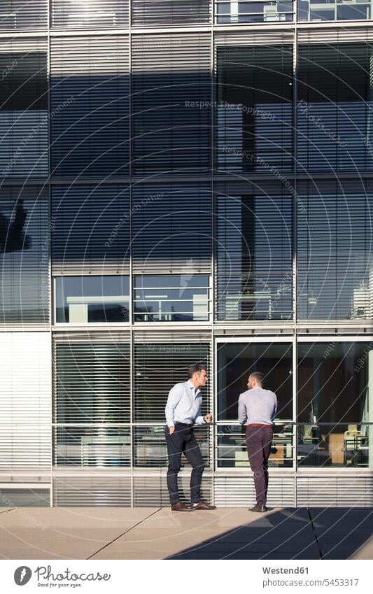 Two businessmen talking outside office building Businessman Business man Businessmen Business men colleagues speaking business people businesspeople