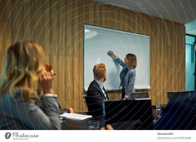 Business people looking at businesswoman writing on whiteboard eyeing business people businesspeople boards businesswomen business woman business women write