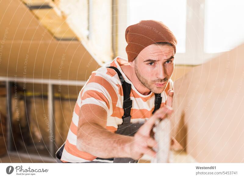 Young man checking plank on construction site home ownership private owned home young man young men carpentry DIY Doityourself Do it yourself Do-it-yourself